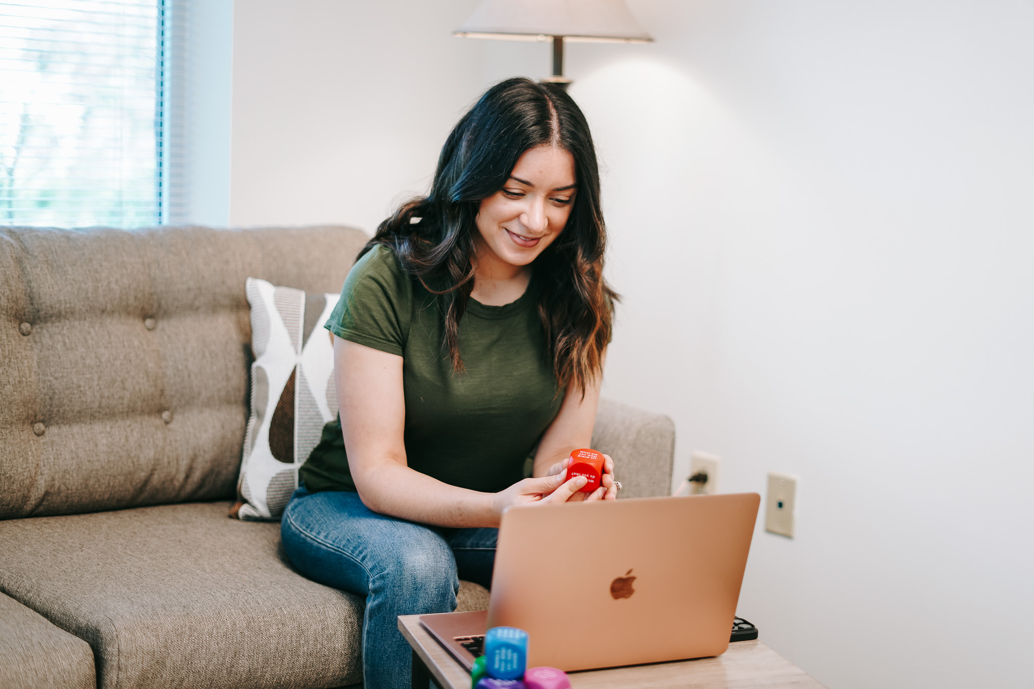 Woman holding a red stress ball while attending an online session from her couch.