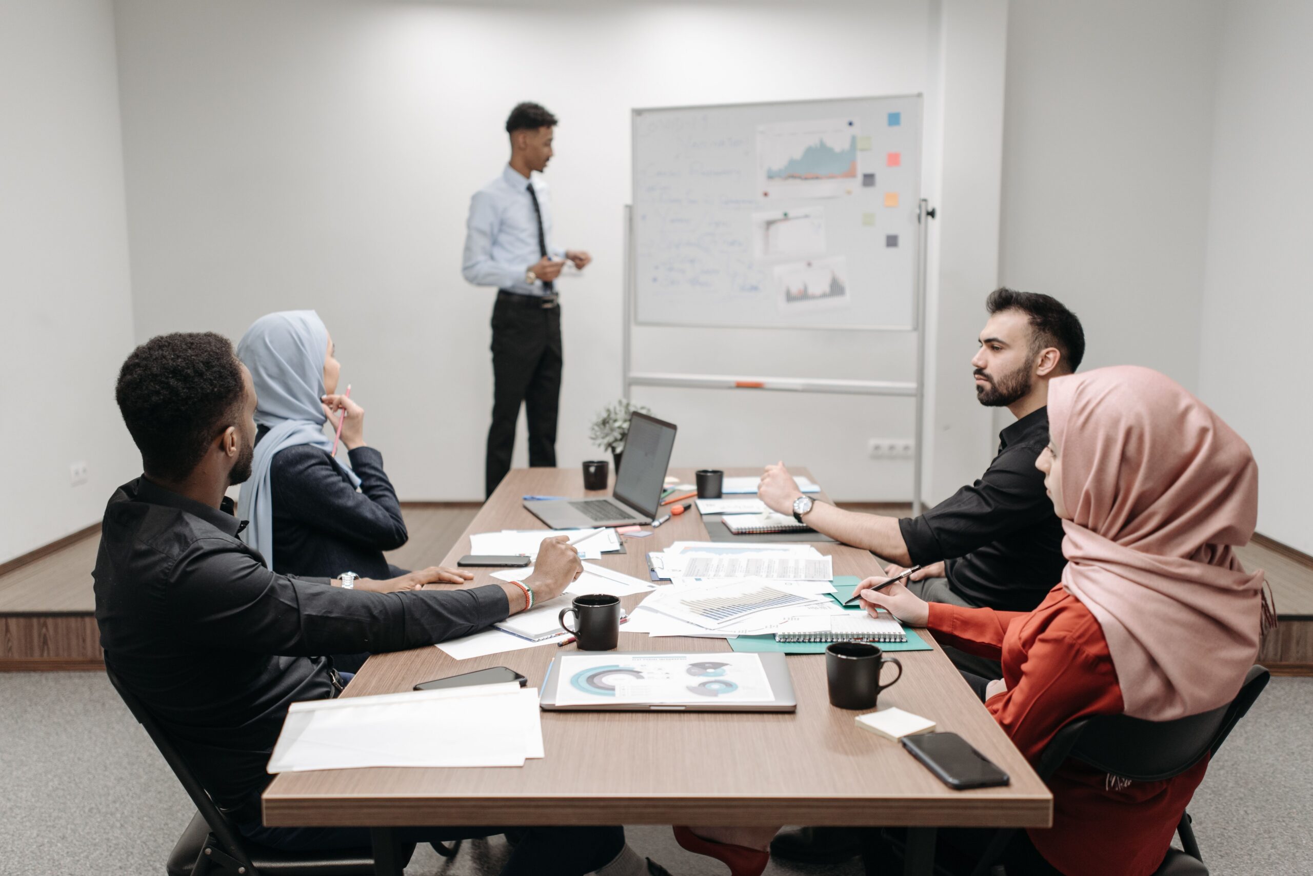 Diverse workplace team listening to a colleague’s presentation during a conference-room meeting.
